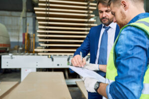 two men writing on paper standing in warehouse